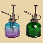 Two glass spray bottles, one blue and one green, on a gray background.